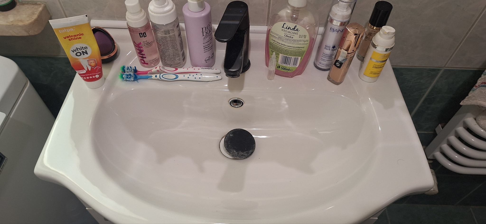 Umywalka w łazience w Krakowie, na której stoją kosmetyki, szczoteczki do zębów i mydło w kostce. Widoczne ślady użytkowania, co sugeruje, że łazienka jest w trakcie użytkowania.
