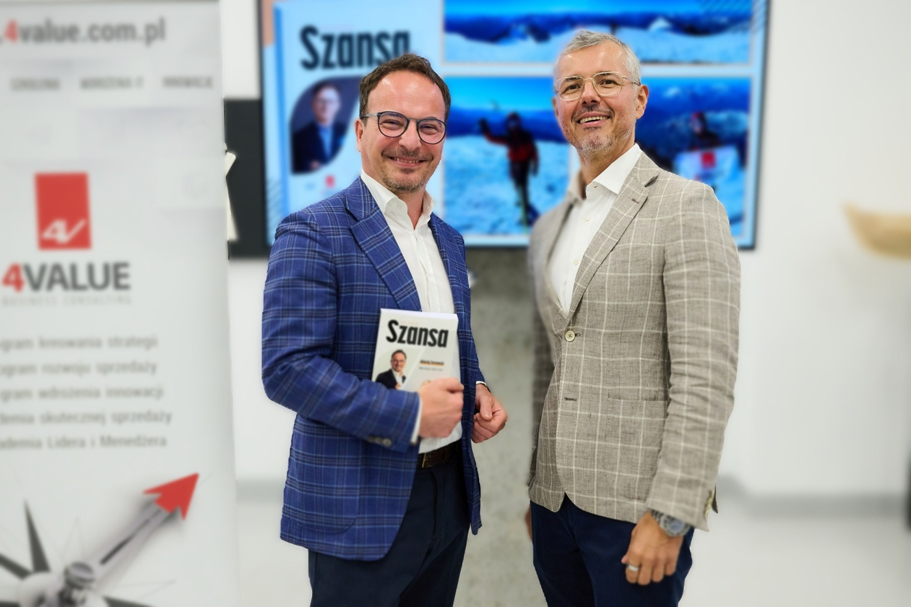 Dwóch uśmiechniętych mężczyzn w marynarkach pozuje z książką 'Szansa' na tle ekranu z zimowymi krajobrazami i logotypu 4Value.pl.