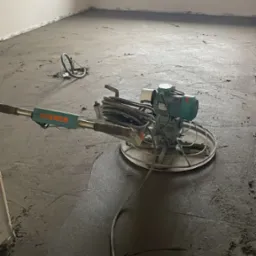 Wygładzanie posadzki jastrychowej w Gorzowie Wielkopolskim za pomocą zacieraczki mechanicznej. Widoczne świeżo wylane podłoże i urządzenie do wygładzania.