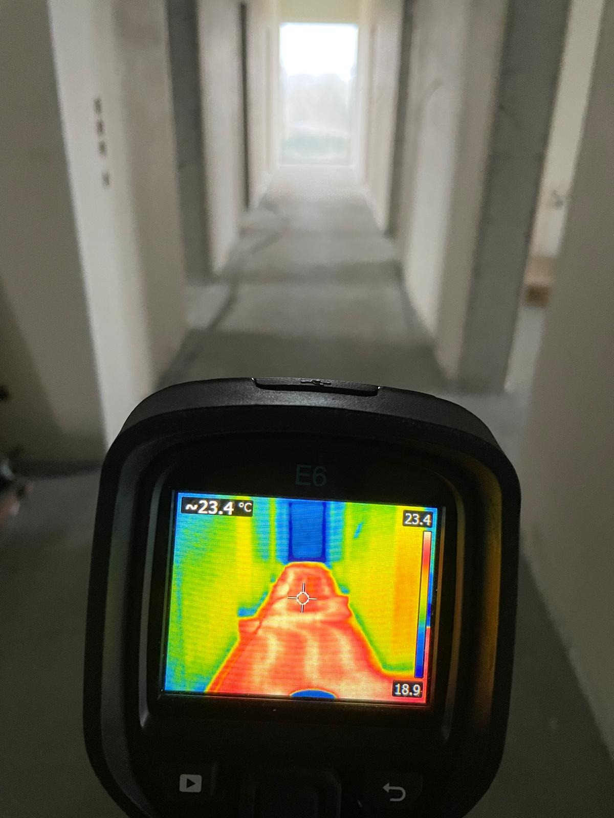 Pomiar termowizyjny posadzki jastrychowej w korytarzu, widoczny na ekranie termowizora E6. Kolory wskazują rozkład temperatur na powierzchni.