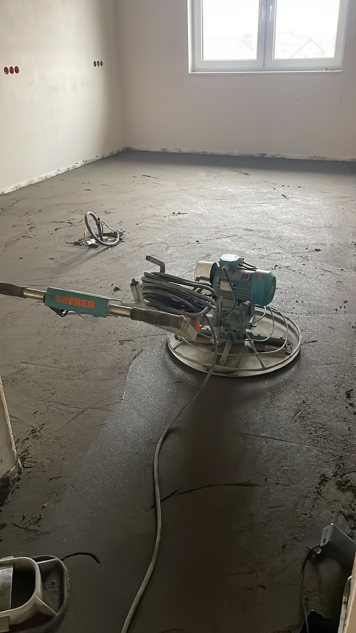 Wygładzanie posadzki jastrychowej w Gorzowie Wielkopolskim za pomocą zacieraczki mechanicznej. Widoczne świeżo wylane podłoże i urządzenie do wygładzania.