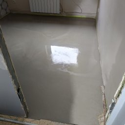 Man-bud - Świeżo wylana, mokra wylewka podłogowa w pomieszczeniu z grzejnikiem. Widoczne przygotowane ściany i podłoże. Ujęcie z góry.