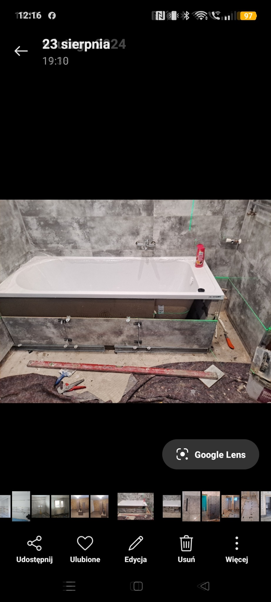 Montaż obudowy wanny w łazience z szarymi płytkami. Widoczne narzędzia, poziomica laserowa i obudowa w trakcie instalacji. Prace glazurnicze w toku.