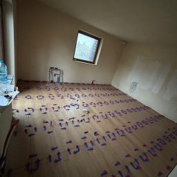 MOTO GASTRO SPÓŁKA Z OGRANICZONĄ ODPOWIEDZIALNOŚCIĄ - Przygotowanie do układania płytek podłogowych w pokoju na poddaszu, z widocznymi krzyżykami dystansowymi i fragmentem instalacji wodnej przy ścianie.