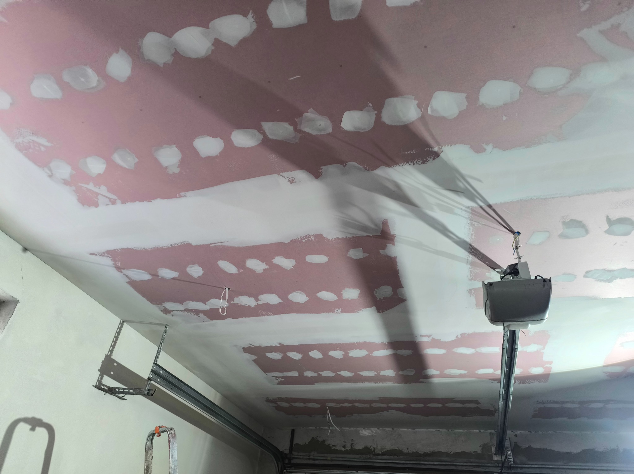 Sufit z płyt kartonowo-gipsowych w trakcie szpachlowania, widoczne łączenia i ślady po wkrętach. Elementy konstrukcyjne garażu w tle.