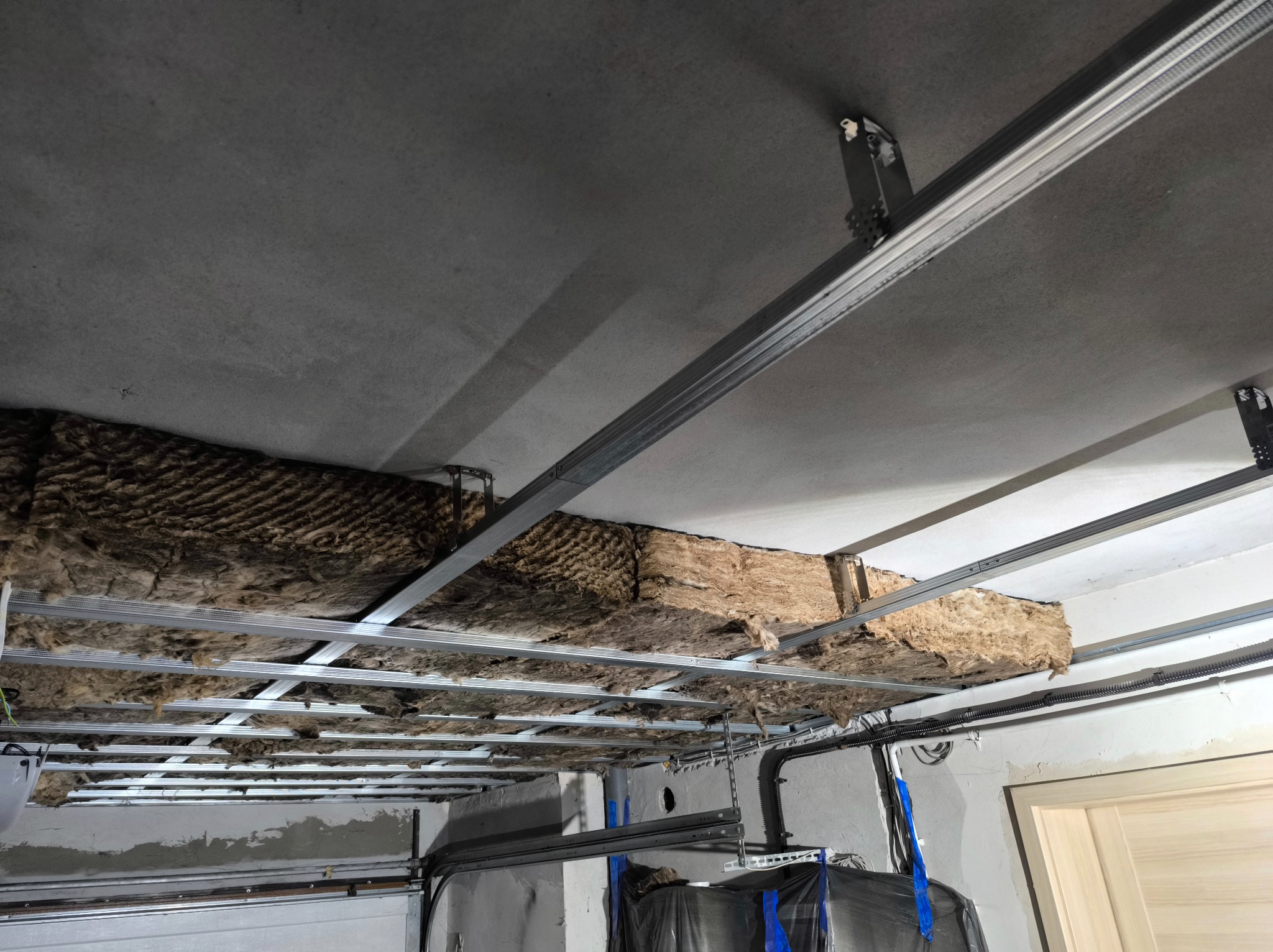 Montaż izolacji z wełny mineralnej na metalowym ruszcie sufitowym w Kałdus. Widoczne przewody elektryczne i fragment ściany. Prace wykończeniowe.