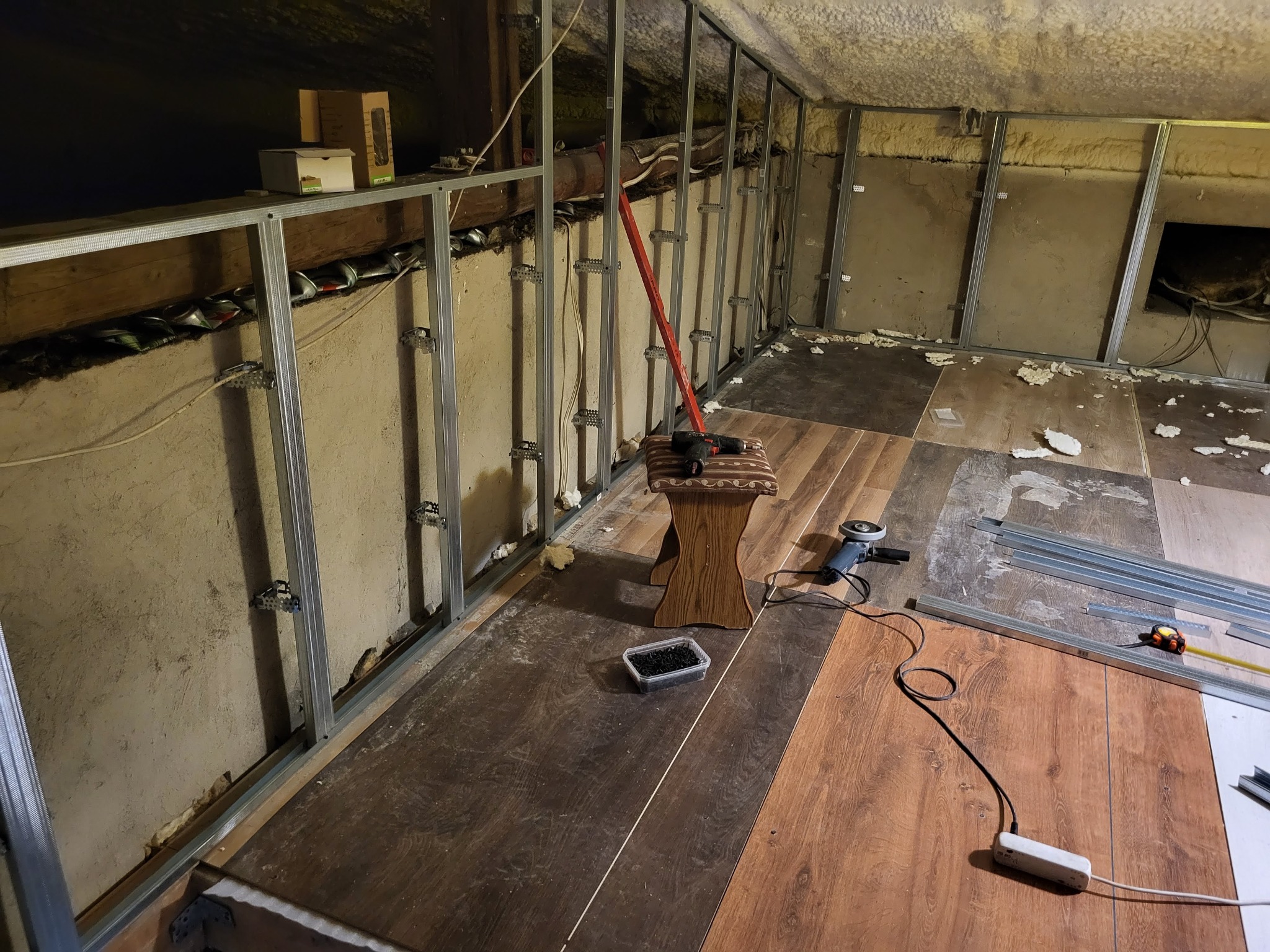 Montaż ścianki działowej z profili metalowych na poddaszu. Widoczne narzędzia, materiały i fragment wykończonej podłogi.