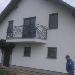 VisionTherm - Biały dom jednorodzinny po remoncie elewacji z balkonem o zdobionej, czarnej balustradzie. Na pierwszym planie mężczyzna w roboczym ubraniu i rower.