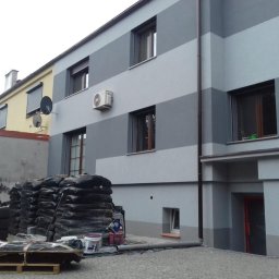 VisionTherm - Ocieplony budynek z szarą elewacją w pasy, widoczne materiały budowlane i narzędzia. Detal: klimatyzator na ścianie.