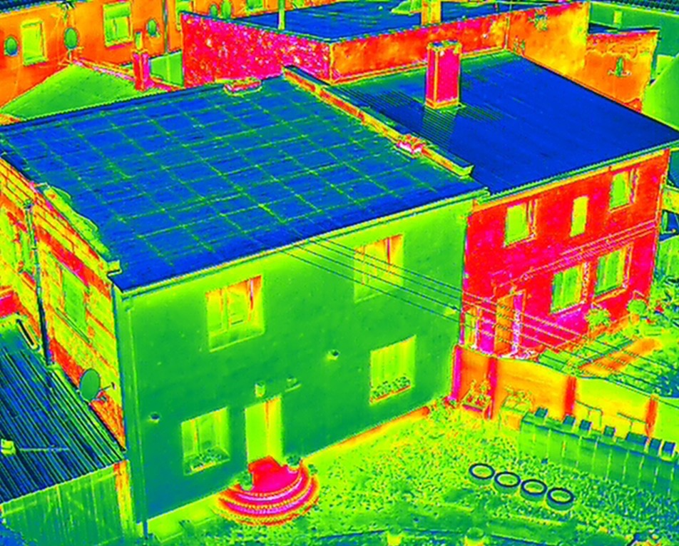 Termowizja dwukondygnacyjnego domu z dachem pokrytym panelami, ukazująca rozkład temperatur ścian i dachu w odcieniach zieleni, czerwieni i niebieskiego.