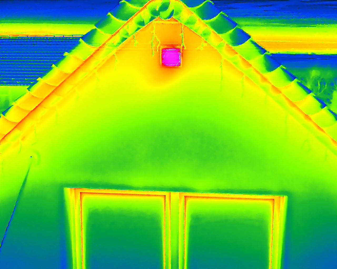 Termowizja fragmentu domu: dach z dachówką, ściana z oknem. Kolory od niebieskiego (zimno) do żółtego i różowego (ciepło) wskazują na straty energii.
