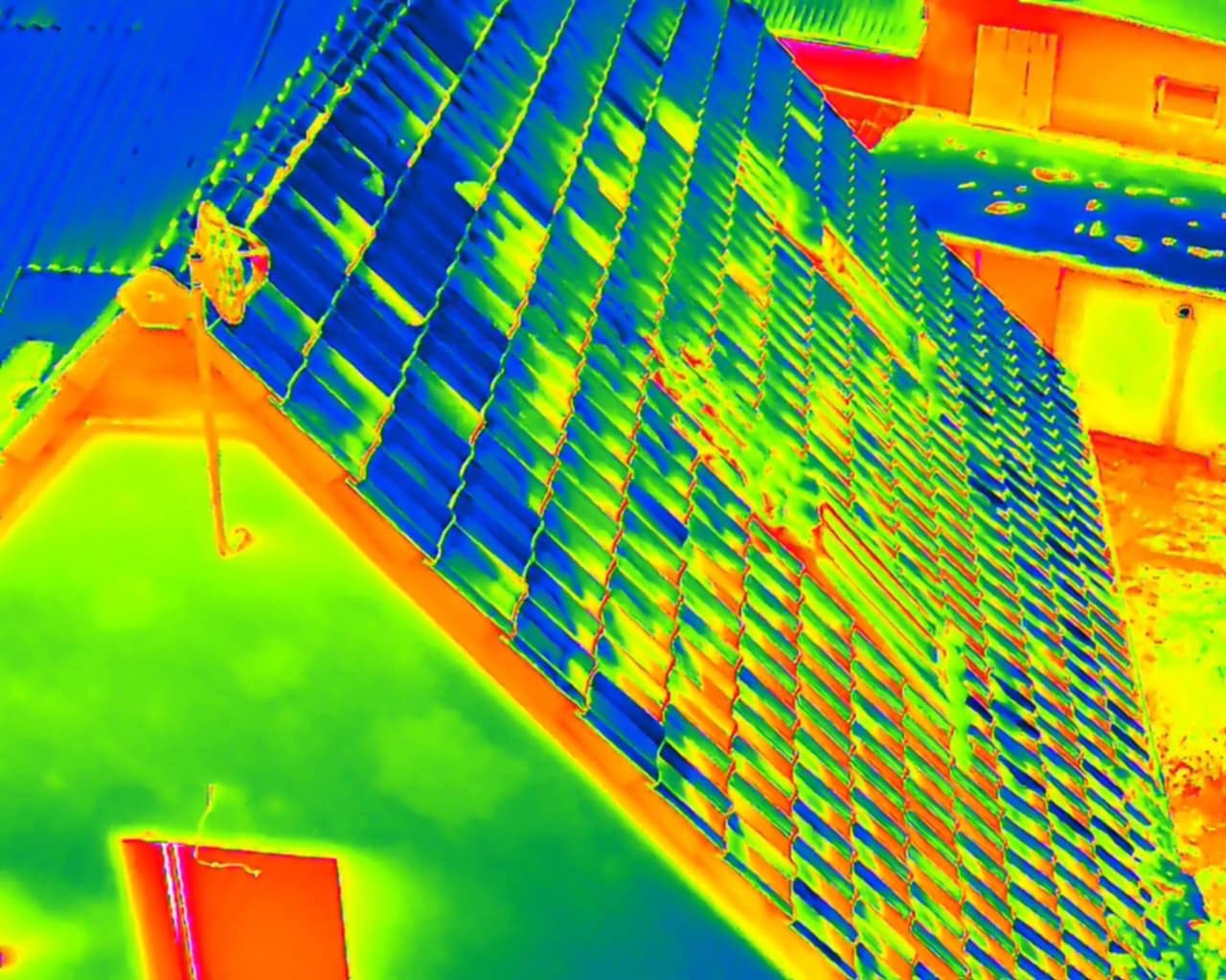 Termowizja dachu budynku z widocznymi różnicami temperatur, ukazująca potencjalne miejsca strat ciepła. Kolorystyka od niebieskiego (zimno) do czerwonego (ciepło).