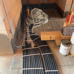 VOLT MASTERS Ernest Wojdyła - Instalacja elektryczna w surowym stanie: wiązki przewodów w peszlach i luźne kable na podłodze, widoczne ściany z cegły.