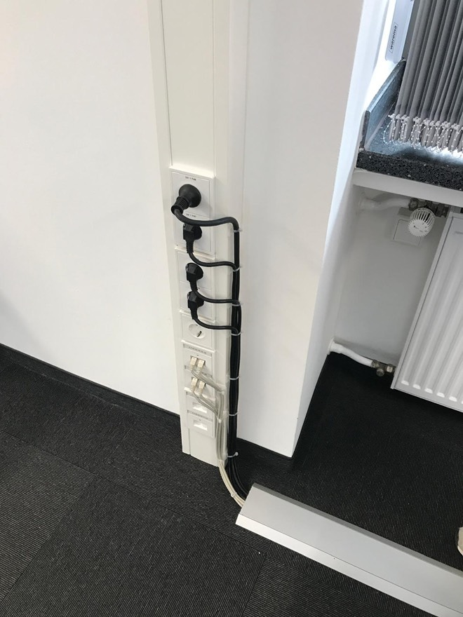 Biała listwa przypodłogowa z gniazdkami i kablami w biurze w Ostrowie. Widoczne gniazda z wtyczkami i porty sieciowe. Estetyczne prowadzenie kabli.