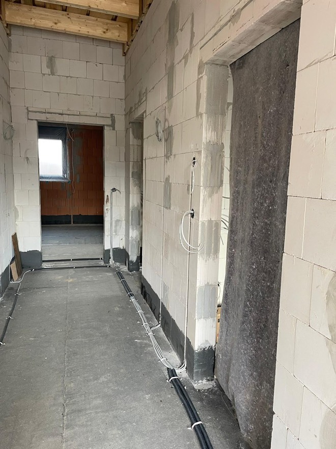 Wnętrze w stanie surowym: ściany z białego betonu komórkowego, widoczne kable elektryczne ułożone wzdłuż podłogi, przygotowane do dalszych prac wykończeniowych.