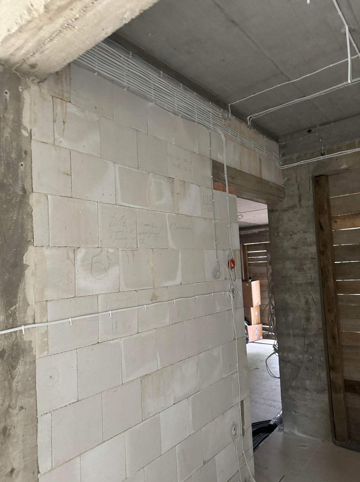 Surowy stan: białe kable elektryczne ułożone wzdłuż ściany z betonu komórkowego, z widocznymi oznaczeniami, w nowym budynku przed wykończeniem.