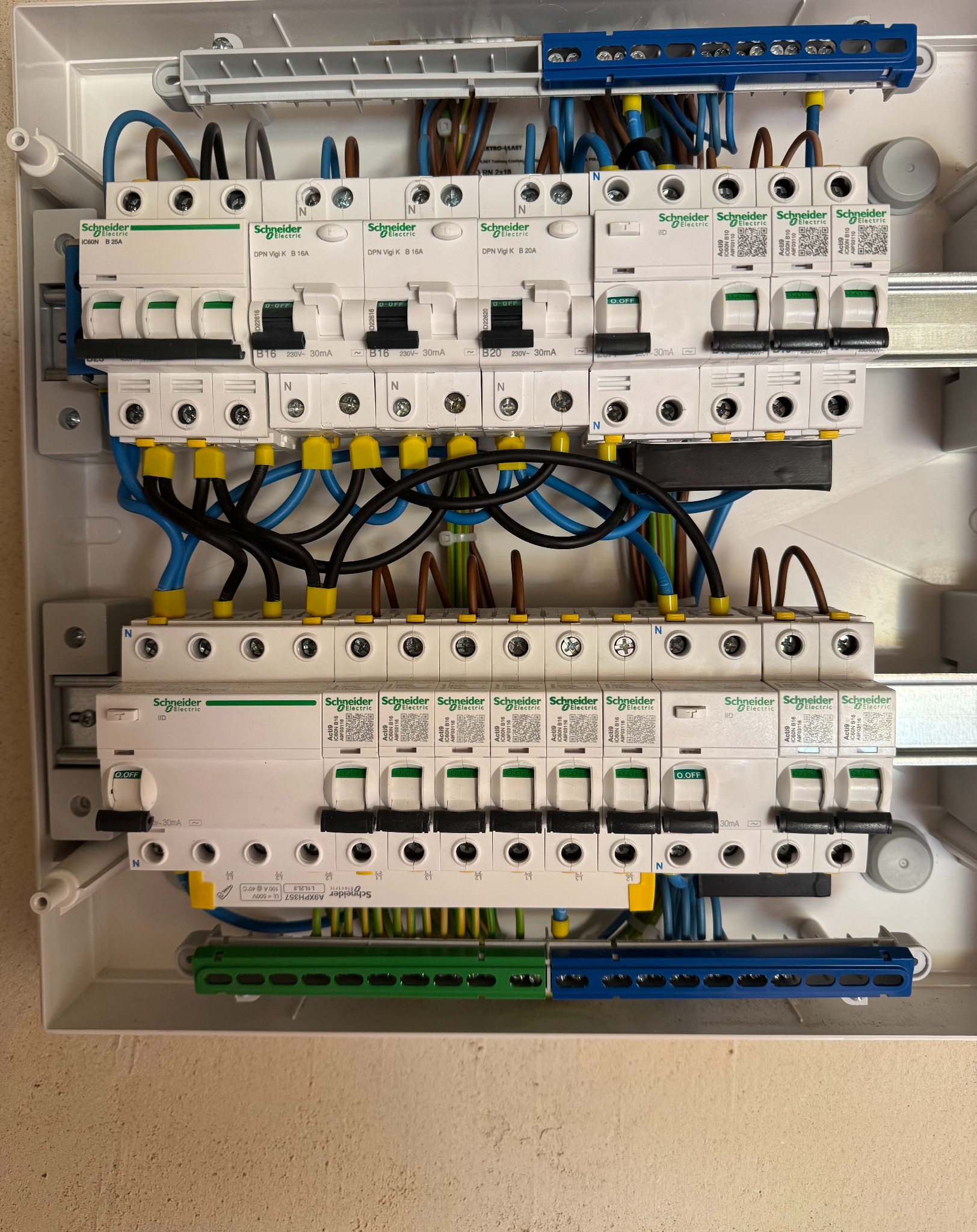 Rozdzielnica elektryczna Schneider Electric z zainstalowanymi bezpiecznikami i przewodami, widoczne kody QR na urządzeniach, całość w białej obudowie.