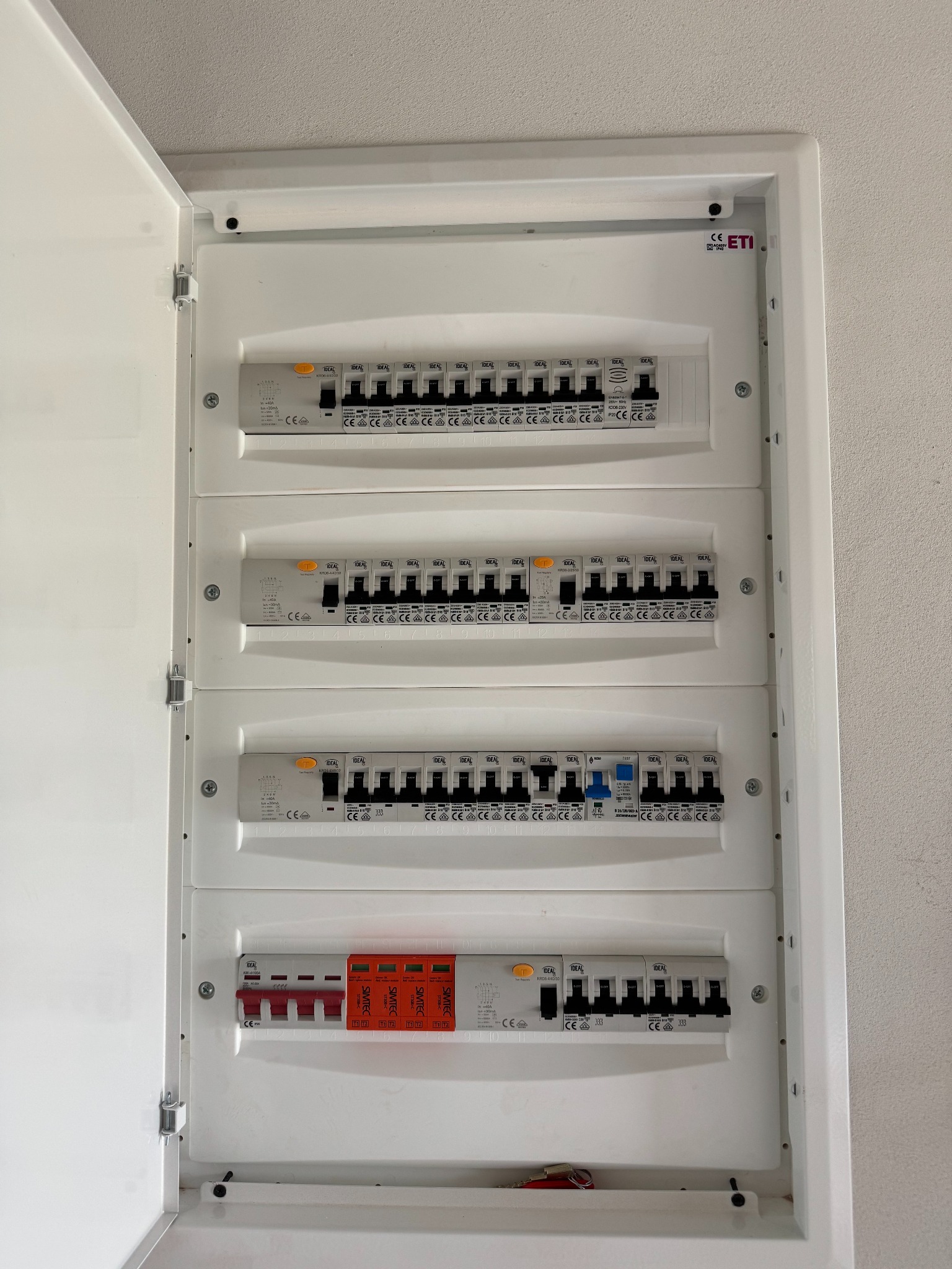 Otwarta skrzynka rozdzielcza z bezpiecznikami i wyłącznikami w mieszkaniu w Warszawie. Widoczne różne typy zabezpieczeń i szyny DIN.