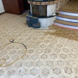 LASER SYSTEM KAMIL WIDAWSKI - Parkiet z wzorem gwiazdy w heksagonach, częściowo odnowiony, z widocznymi materiałami ściernymi obok kominka i zabezpieczonymi schodami. Widoczny kabel od maszyny.