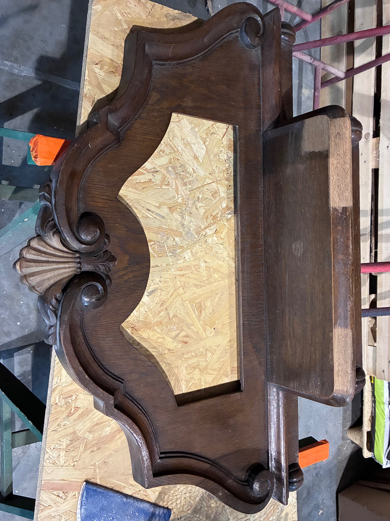 Renowacja ramy lustra: ozdobna, ciemna rama z drewna, częściowo odnowiona, leży na płycie OSB. Widoczne ślady obróbki i zaciski.