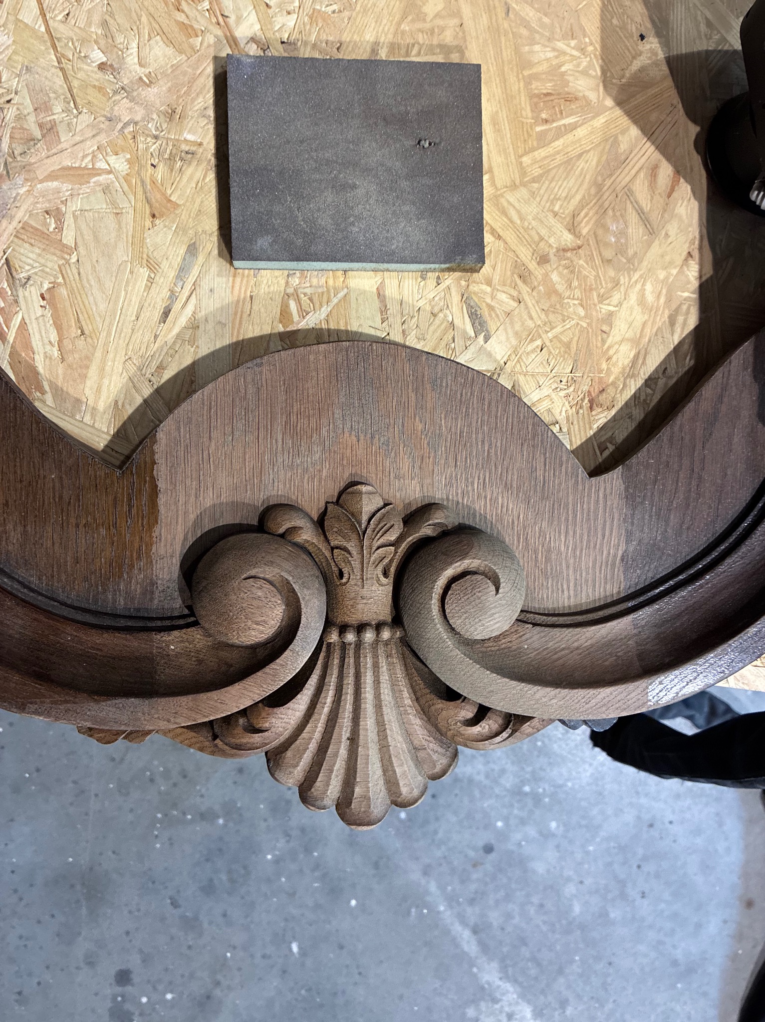 Fragment ramy z drewna podczas renowacji w Pszczynie, widoczny ornament i gąbka ścierna. Częściowo odnowiona powierzchnia ukazuje różnicę w kolorze.