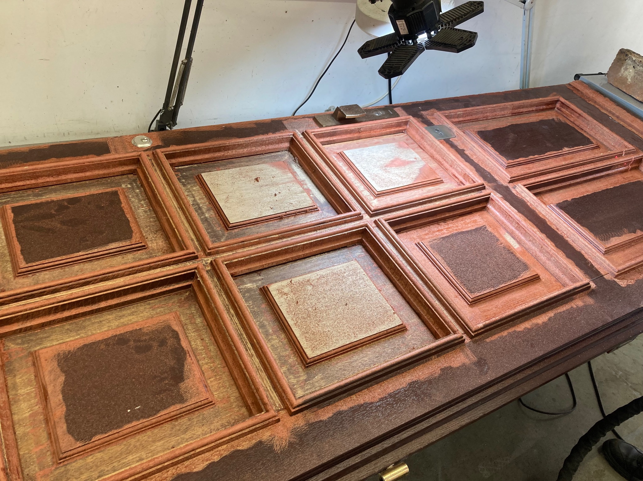 Renowacja drewnianych drzwi kasetonowych z widocznymi śladami farby i szlifowania, ukazująca proces odnawiania powierzchni w warsztacie.