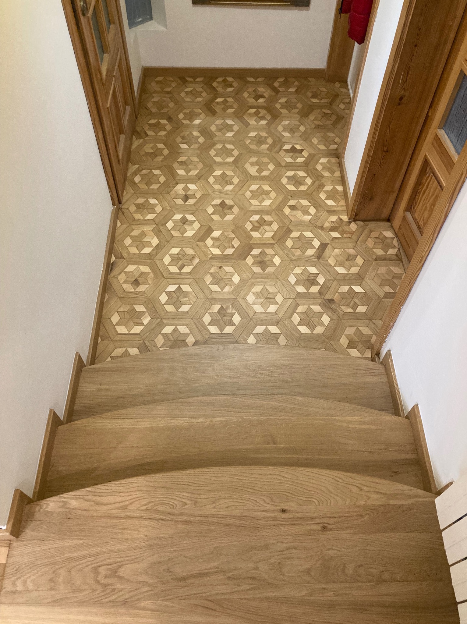 Wykończone drewniane schody z parkietem ułożonym w geometryczny wzór, widok z góry. Jasne drewno, naturalne oświetlenie.