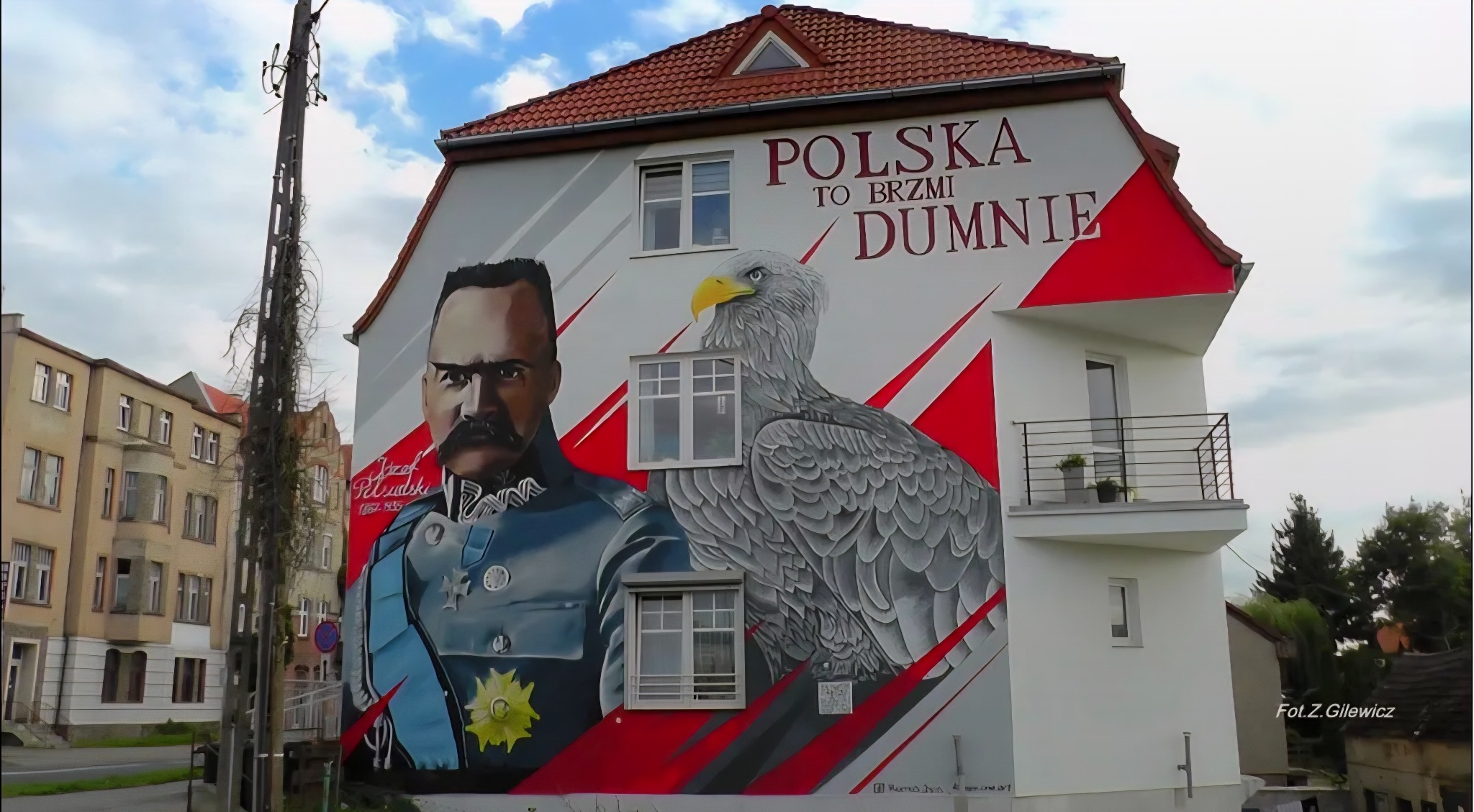 Mural na ścianie budynku z portretem Józefa Piłsudskiego i orłem w barwach narodowych z napisem: 'Polska to brzmi dumnie'.