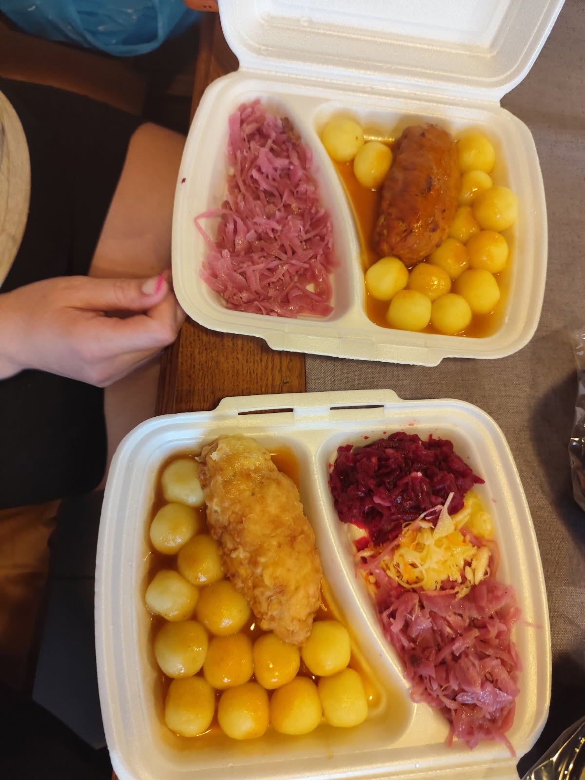 Dwa zestawy obiadowe w styropianowych pojemnikach: kotlet, ziemniaki w sosie i surówki z czerwonej i białej kapusty, gotowe do spożycia.