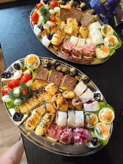 Dwie srebrne tace z różnorodnymi przekąskami: kanapkami, roladkami, tartaletkami i warzywami. Idealne na elegancki catering.