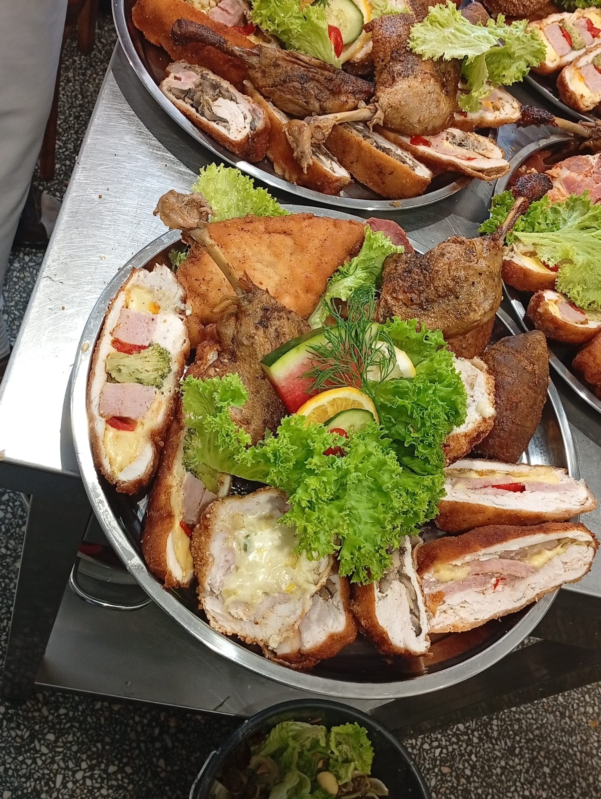 Srebrna patera z pieczonymi udkami, roladkami z nadzieniem i świeżą sałatą, dekorowana cytrusami i ogórkiem.