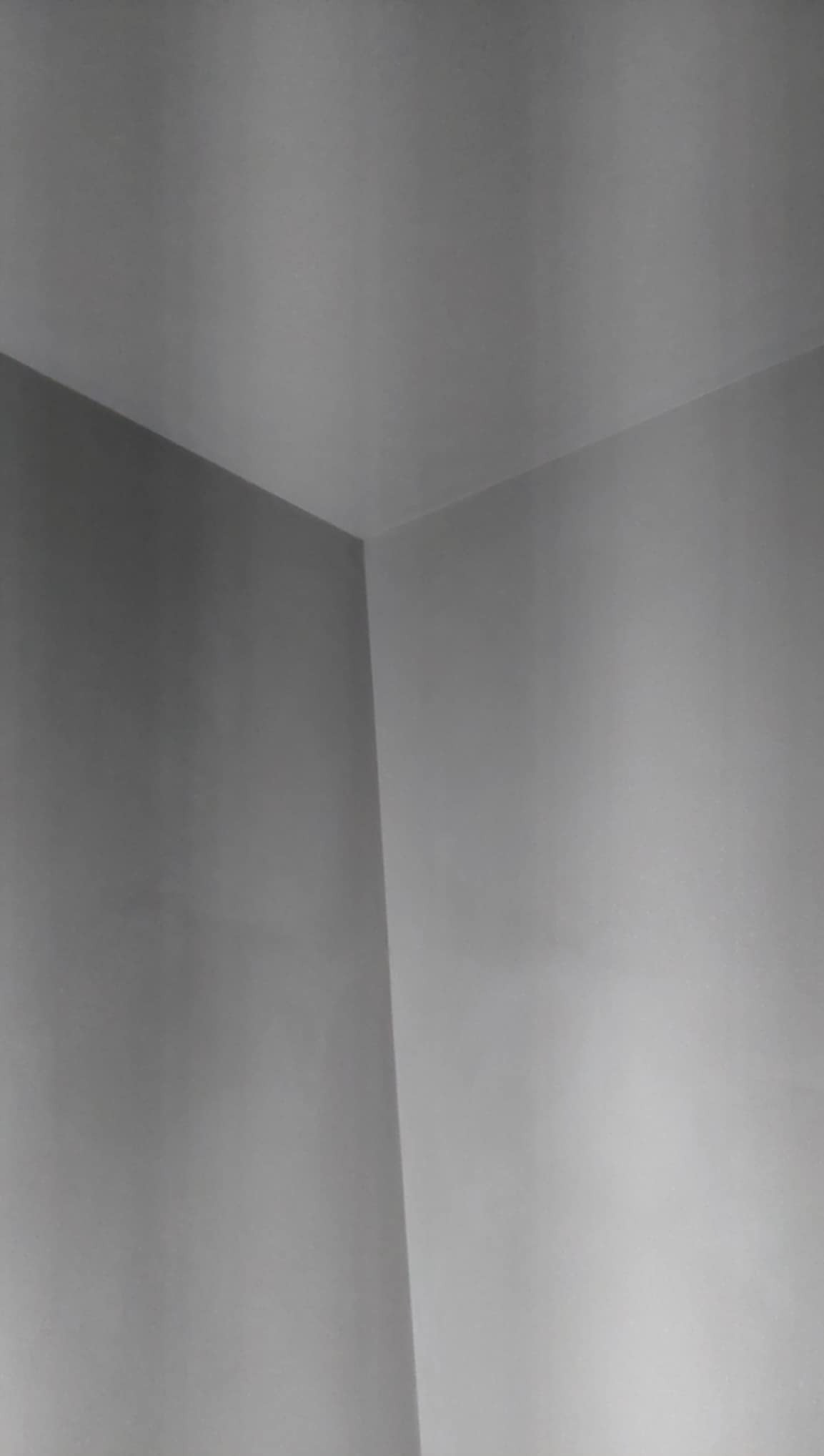 Gładkie, szare ściany i sufit w rogu pokoju, świeżo po położeniu tynków. Delikatne przejścia tonalne podkreślają równość powierzchni. Minimalistyczne ujęcie.