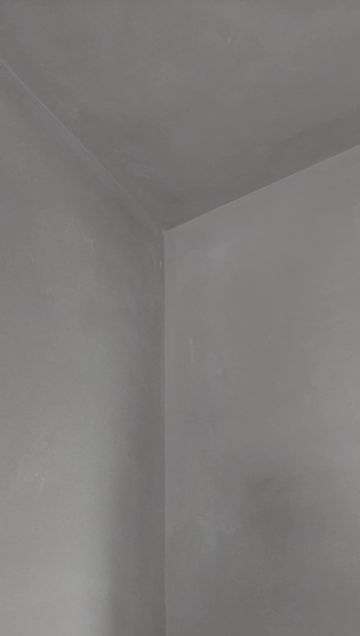 Gładkie, szare ściany i sufit po nałożeniu tynku maszynowego, widoczne w rogu pomieszczenia. Minimalistyczne ujęcie, skupiające się na fakturze i wykończeniu powierzchni.