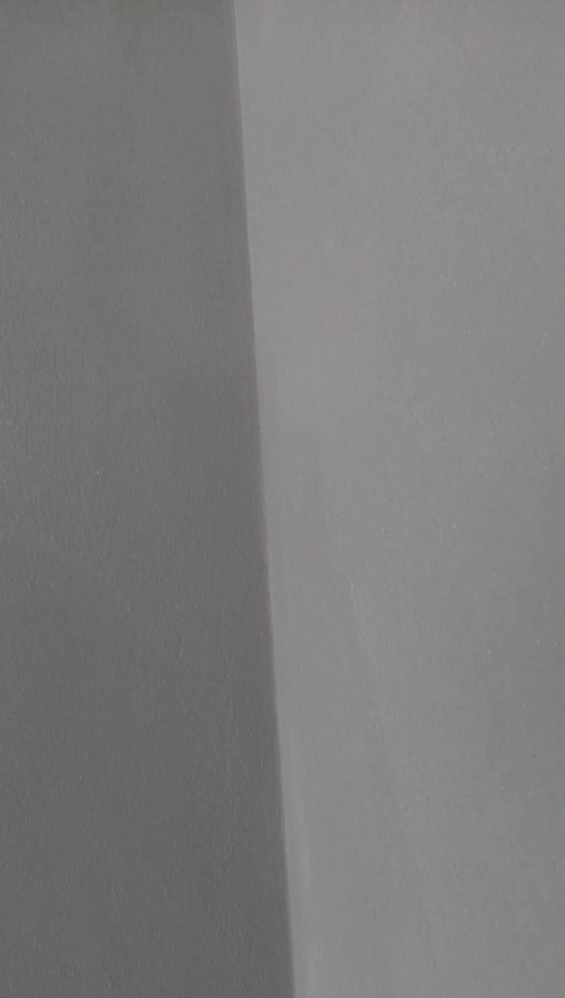 Gładka, szara ściana w rogu pomieszczenia z delikatną fakturą, ukazująca precyzyjne wykończenie powierzchni po tynkowaniu. Minimalistyczne ujęcie detalu.