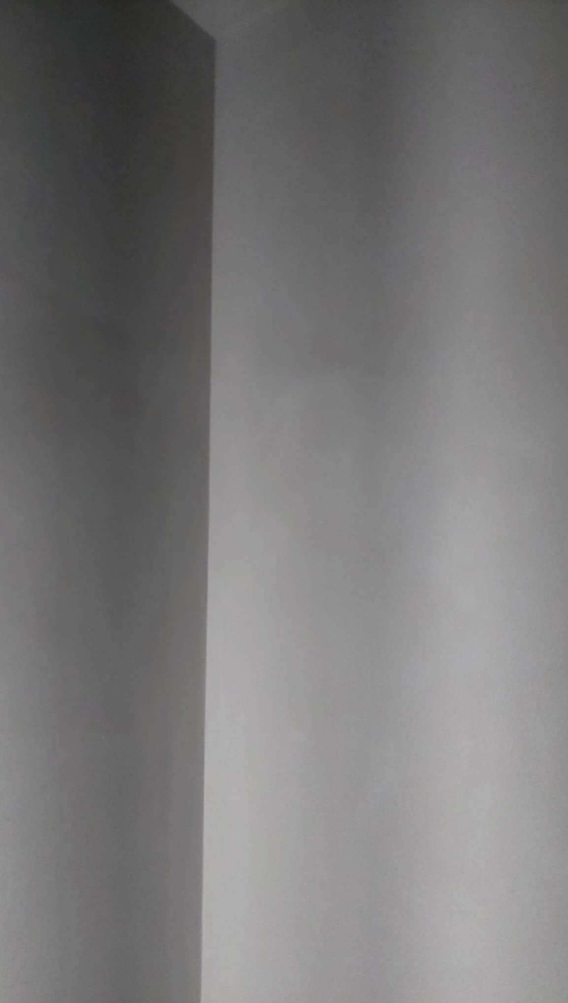 Gładka, szara ściana po tynkowaniu maszynowym, widoczny róg pomieszczenia. Minimalistyczne ujęcie, delikatne światło podkreśla strukturę.