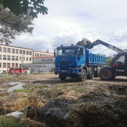 VOS Rafał Osadnik - Niebieska ciężarówka Iveco i ładowarka Bobcat na placu budowy. Widoczne wykopy pod fundamenty i budynek w tle. Praca w toku.