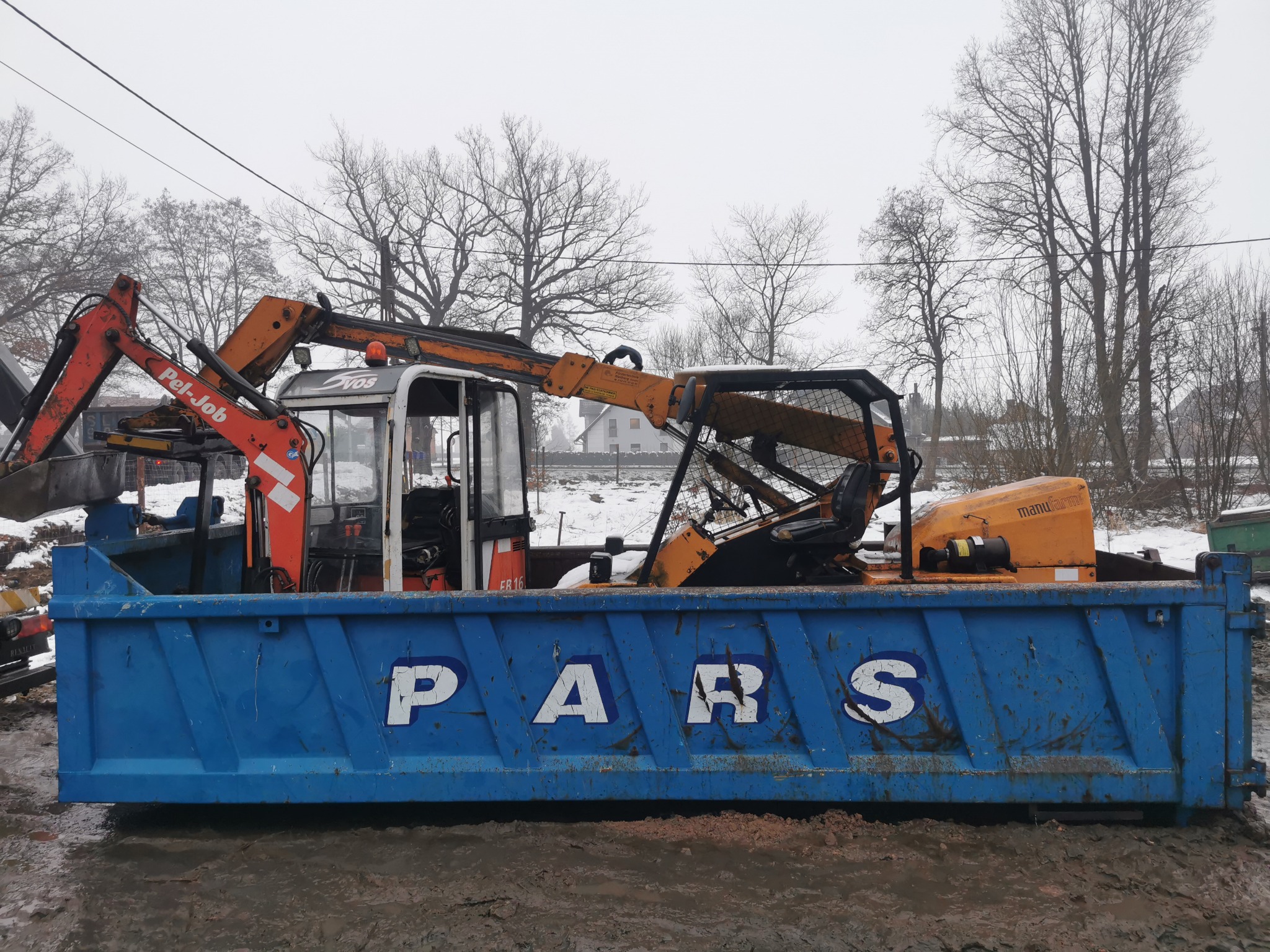 Żuraw przenośny Pel-Job i Manu-Farm na niebieskiej przyczepie Pars, w tle zimowy krajobraz z drzewami bez liści i zabudowaniami.