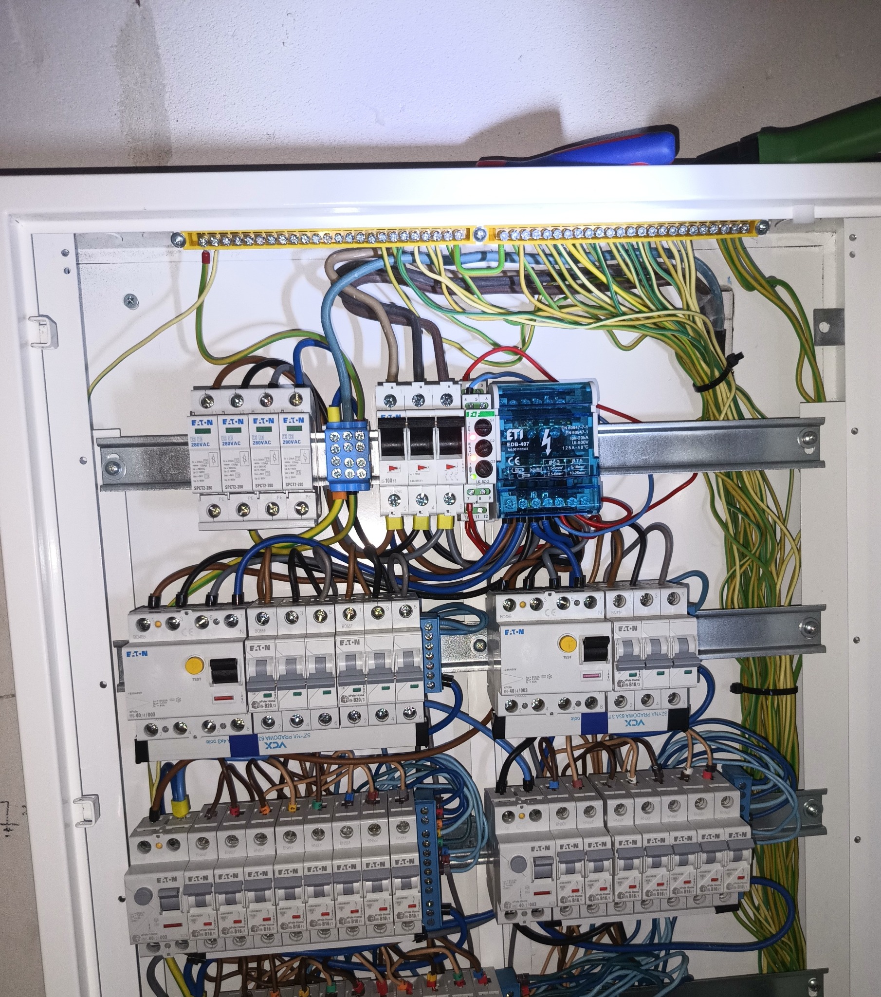 Rozdzielnica elektryczna z zainstalowanymi zabezpieczeniami EATON, widoczne kable i listwy zaciskowe. Całość w białej obudowie.
