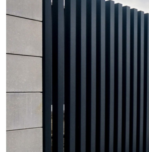 Nowoczesne ogrodzenie z pionowych, grafitowych metalowych profili, przylegające do betonowego murku z szarych bloczków. Minimalistyczny design.