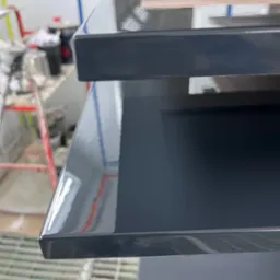 Błyszczące, świeżo polakierowane fronty meblowe w odcieniach szarości, ułożone jeden na drugim w lakierni. Widoczne odbicia światła i drobne niedoskonałości powierzchni.