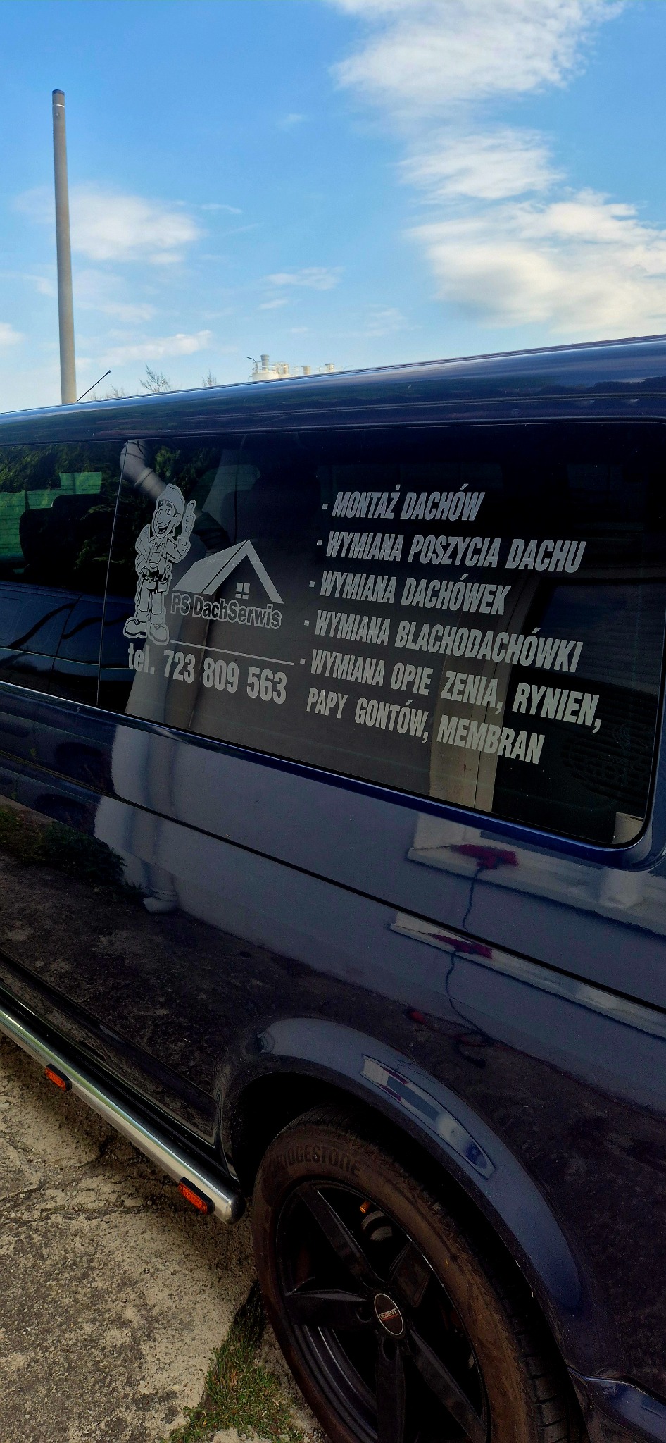 Granatowy bus z naklejkami firmy dekarskiej 'PS DachSerwis' oferującej m.in. montaż i wymianę dachów, poszycia, dachówek, rynien i papy gontowej. Widoczny numer telefonu.