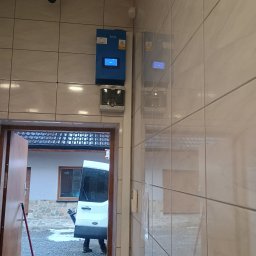 M-tech Mateusz Kasperkiewicz - Montaż skrzynki elektrycznej Savio na kafelkowanej ścianie. Widoczny także biały samochód dostawczy Ford za otwartymi drzwiami. Instalacja monitoringu.