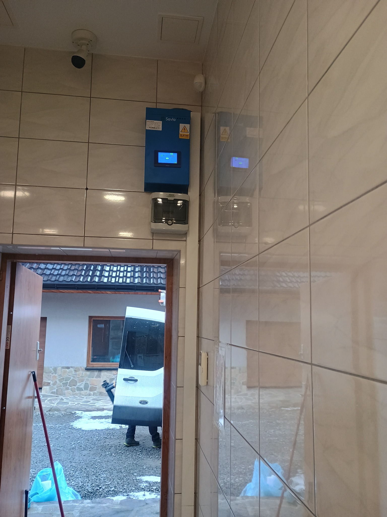 Montaż skrzynki elektrycznej Savio na kafelkowanej ścianie. Widoczny także biały samochód dostawczy Ford za otwartymi drzwiami. Instalacja monitoringu.