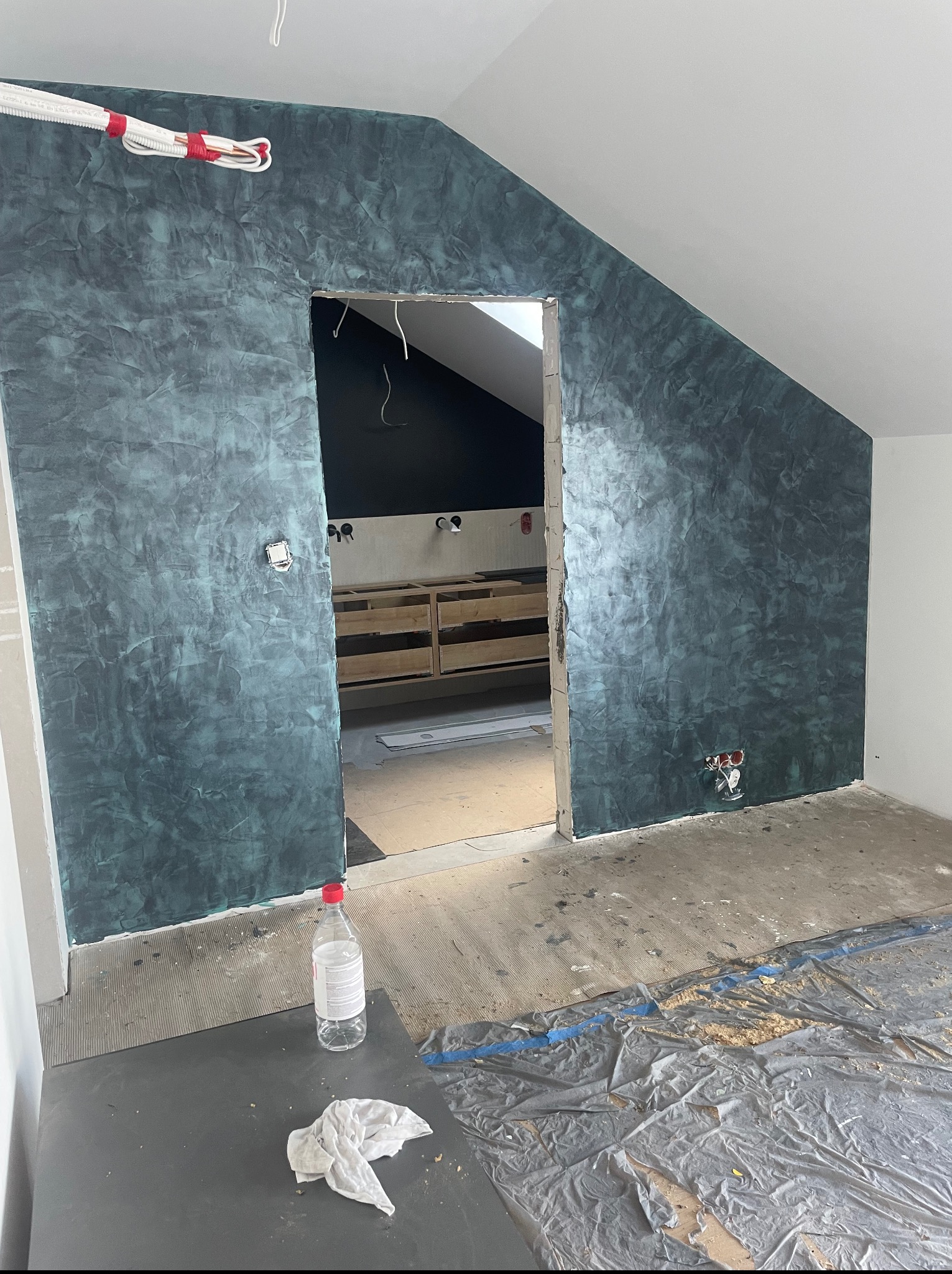 Wykończone ściany w odcieniach turkusu w pokoju na poddaszu, widoczne instalacje elektryczne i przygotowania do dalszych prac wykończeniowych.