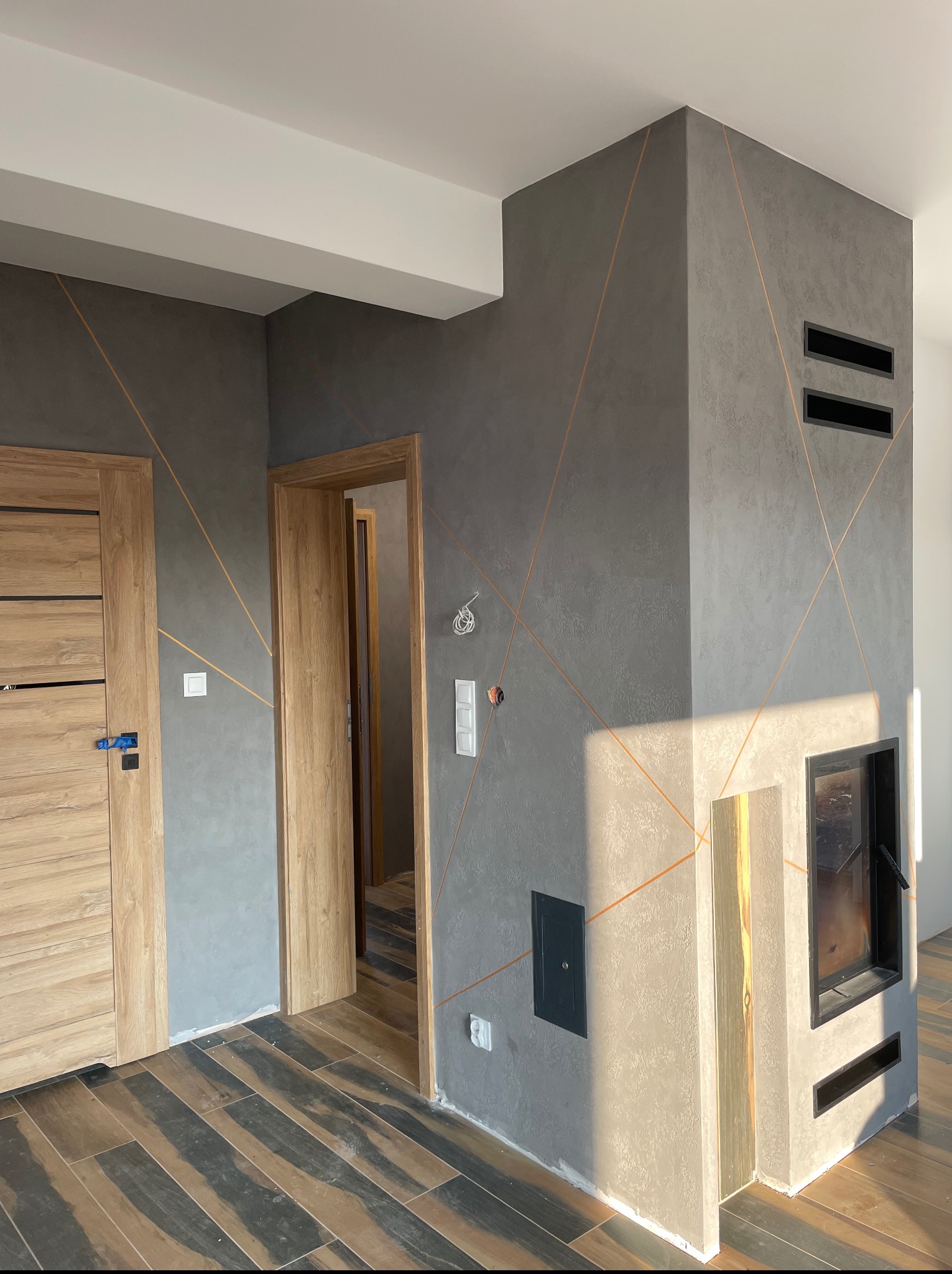 Szara ściana z dekoracyjnymi liniami i kominkiem, drewniane drzwi i podłoga z płytek. Elementy wykończenia wnętrz w nowoczesnym stylu.