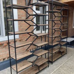 Dwie metalowe półki w stylu loft z drewnianymi blatami na tle ceglanej ściany i okna. Unikalny wzór metalowej konstrukcji w kształcie zygzaka.