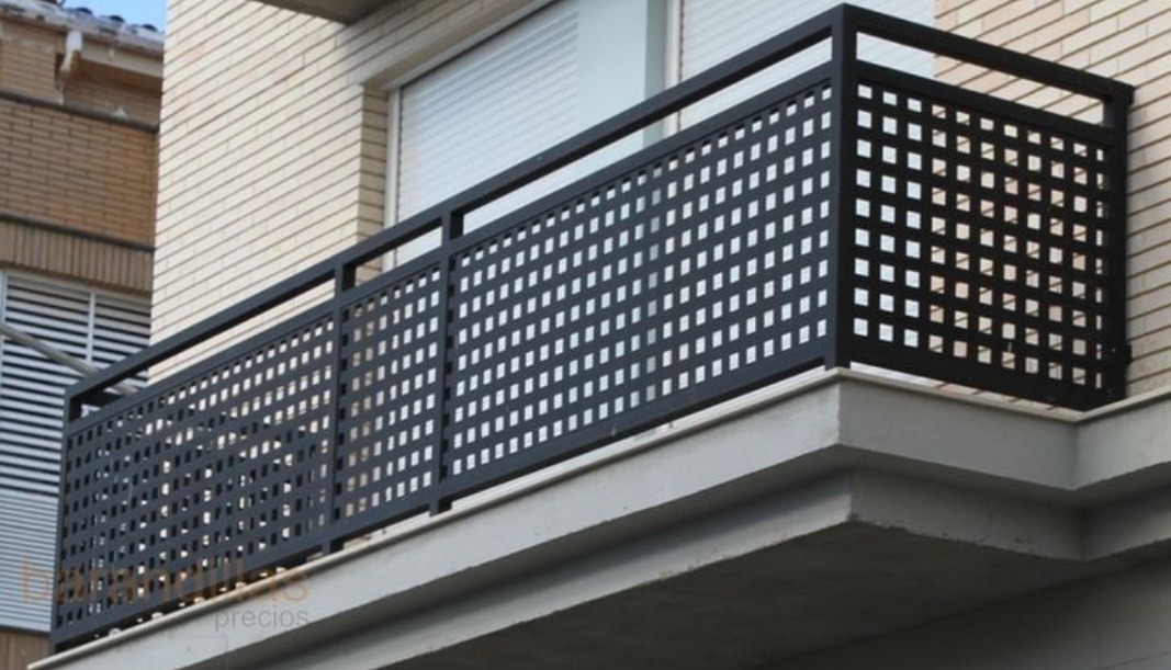 Czarna, metalowa balustrada balkonowa z ażurowym wypełnieniem w kwadraty, zamontowana na balkonie budynku z jasnej cegły.