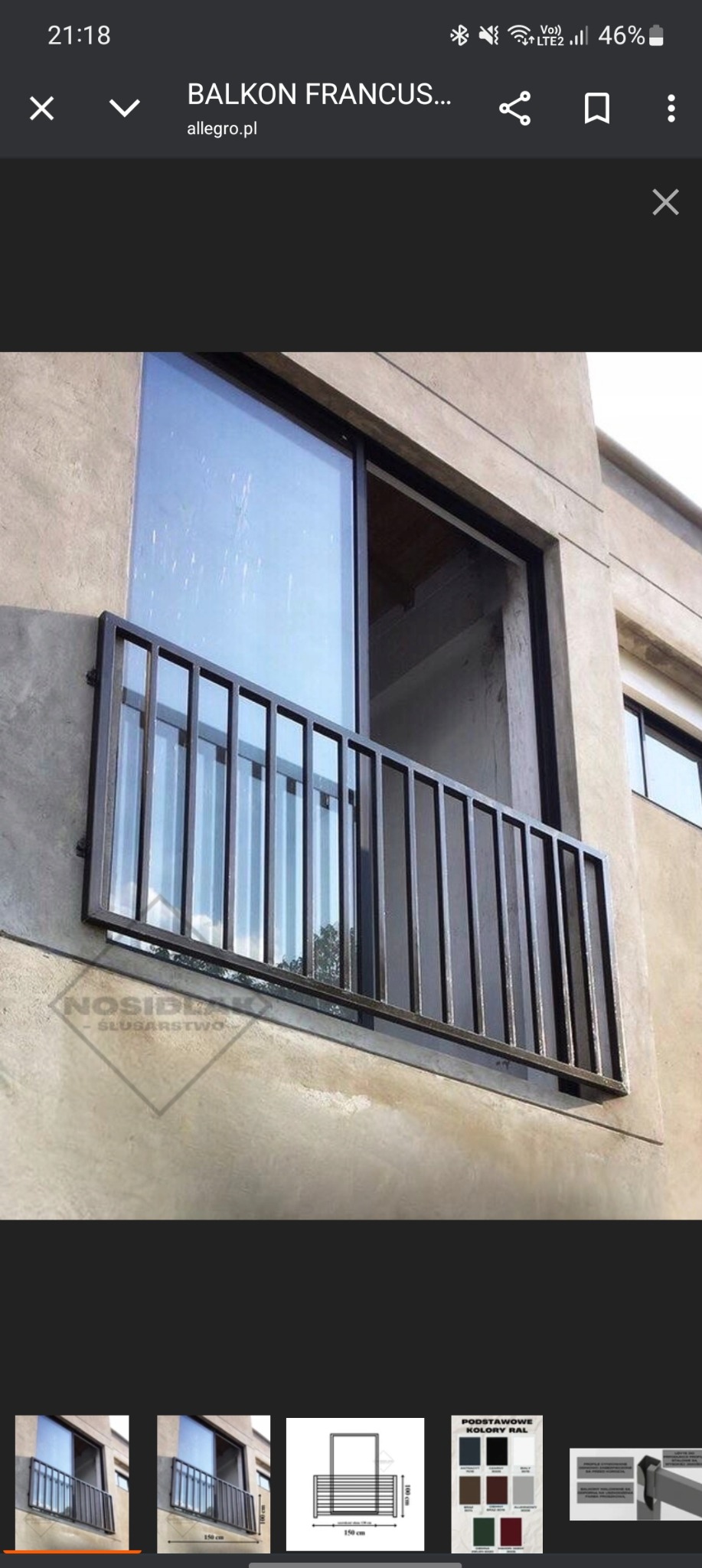 Metalowa balustrada balkonu francuskiego, widoczna z zewnątrz, z pionowymi szczebelkami i gładką, szarą fasadą budynku w tle. Ujęcie z dołu.