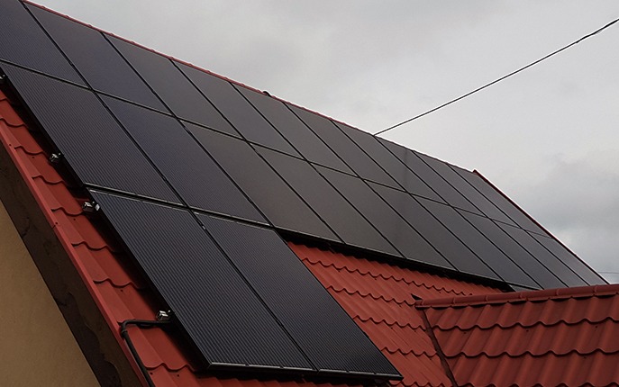 Panele fotowoltaiczne na dachu z czerwonej dachówki w Opalenicy. Widok pod kątem, pochmurne niebo w tle. Instalacja solarna.