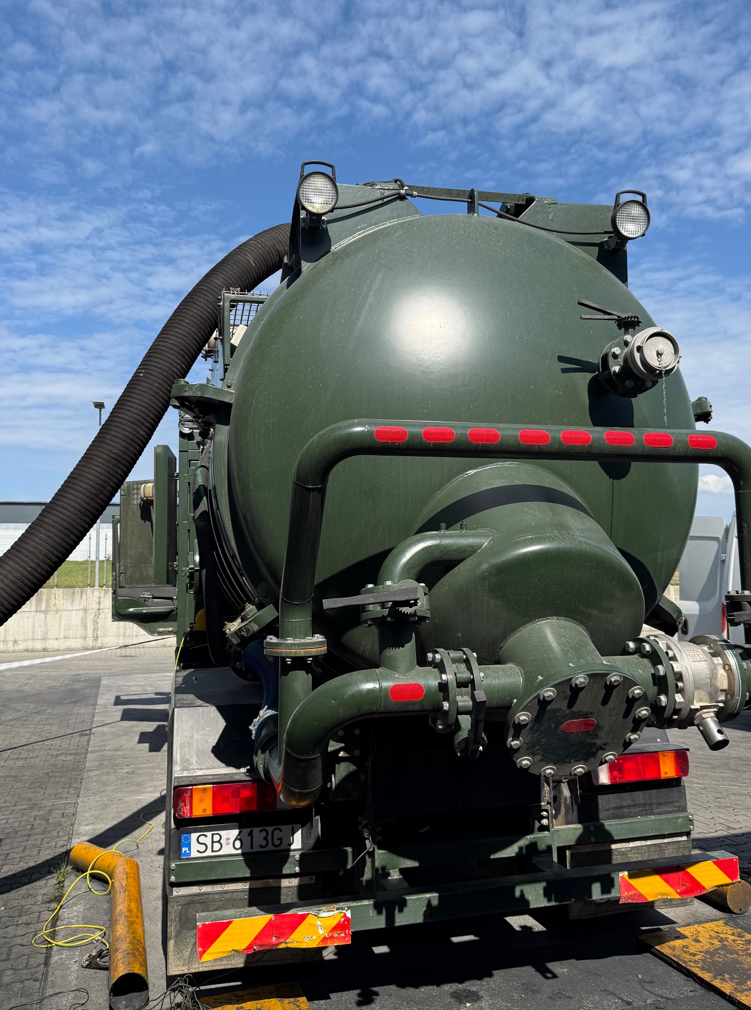 Wóz asenizacyjny w Bielsko-Białej: widok z tyłu, duży zbiornik w kolorze khaki, czarny wąż ssący, światła ostrzegawcze, tablica rejestracyjna. Sprzęt do czyszczenia.